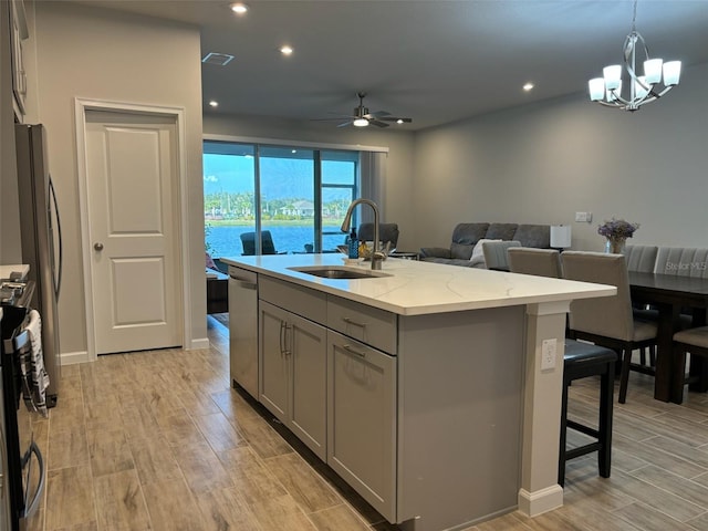 kitchen with a kitchen island with sink, gray cabinetry, sink, light stone countertops, and light wood-type flooring