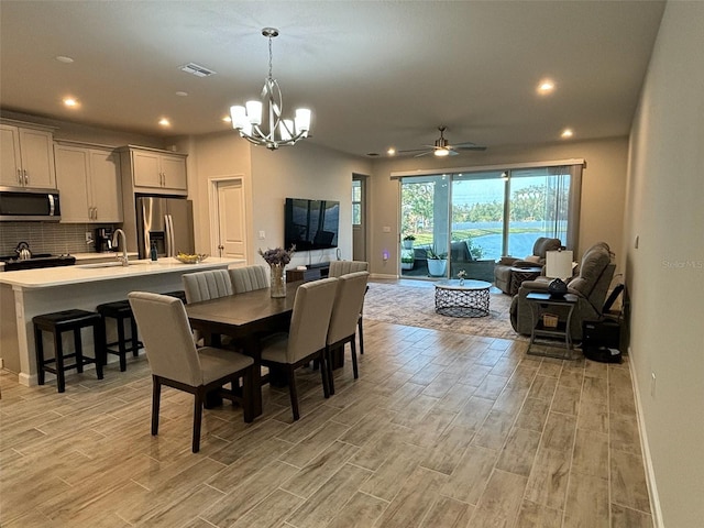 dining space with sink, ceiling fan with notable chandelier, and light wood-type flooring