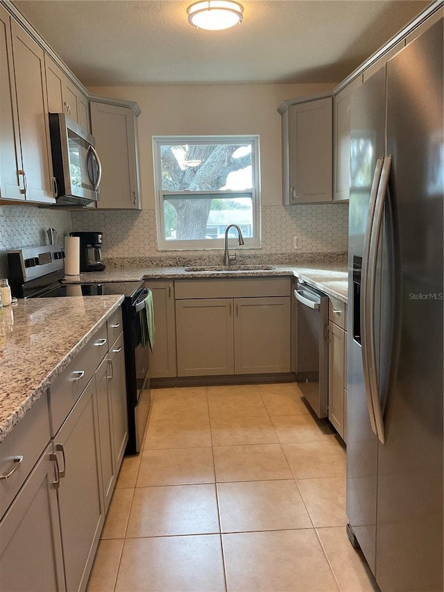 kitchen with light tile patterned flooring, sink, light stone counters, appliances with stainless steel finishes, and tasteful backsplash