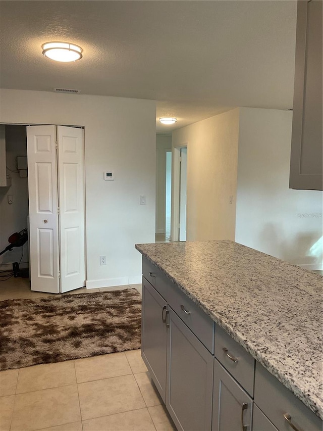 kitchen featuring gray cabinets, a textured ceiling, light stone counters, and light tile patterned floors