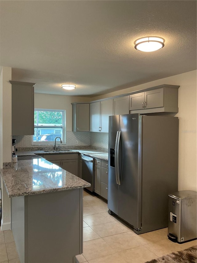 kitchen featuring stainless steel appliances, light stone counters, kitchen peninsula, sink, and gray cabinetry