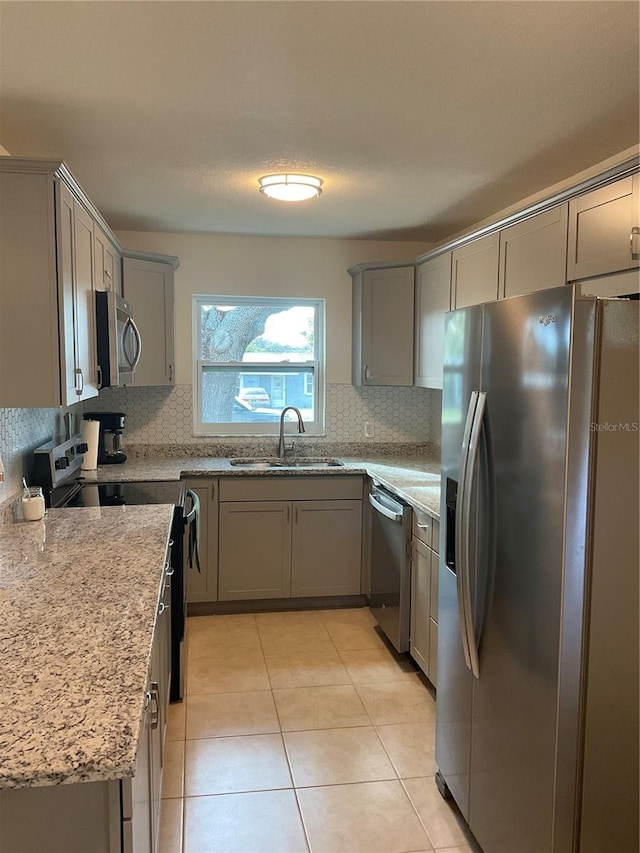 kitchen with tasteful backsplash, light stone counters, light tile patterned flooring, appliances with stainless steel finishes, and sink