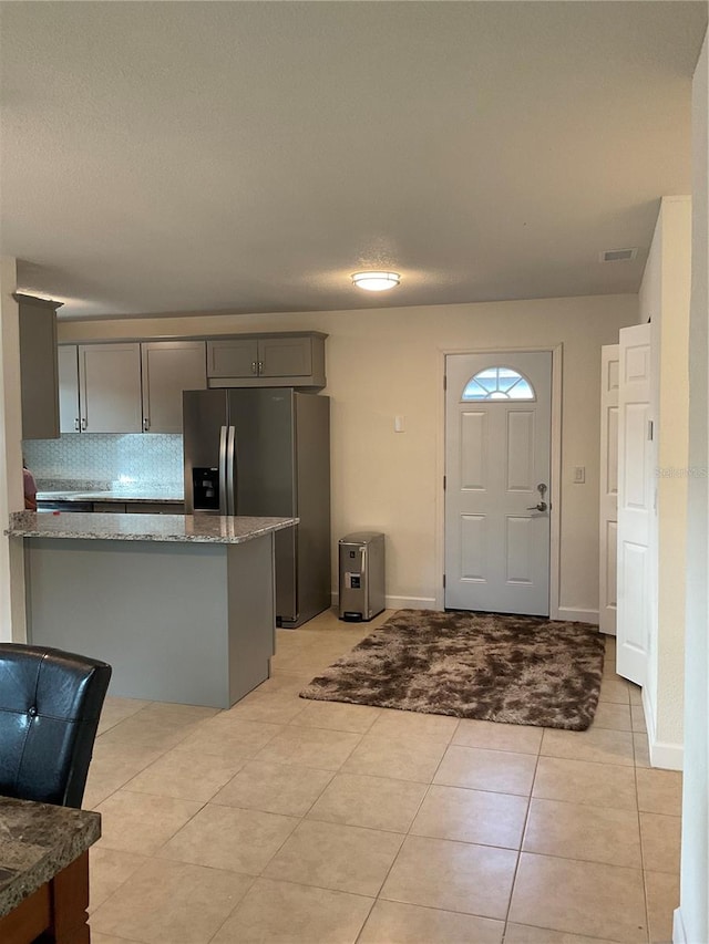 kitchen with kitchen peninsula, stainless steel fridge with ice dispenser, gray cabinets, light tile patterned flooring, and light stone countertops