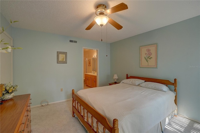 bedroom featuring a textured ceiling, ensuite bathroom, light colored carpet, and ceiling fan