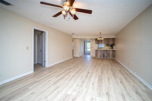 unfurnished living room featuring visible vents, baseboards, a textured ceiling, light wood finished floors, and ceiling fan with notable chandelier