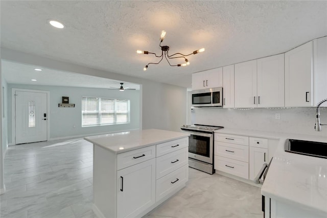 kitchen with white cabinetry, sink, a kitchen island, ceiling fan with notable chandelier, and appliances with stainless steel finishes