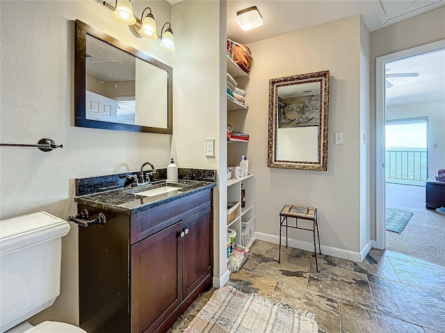 bathroom featuring stone finish flooring, vanity, toilet, and baseboards