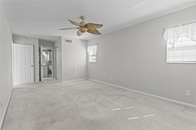 spare room with a textured ceiling, light colored carpet, and ceiling fan