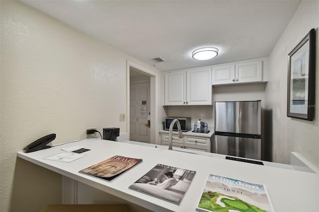 kitchen with a textured ceiling, white cabinetry, kitchen peninsula, and stainless steel appliances