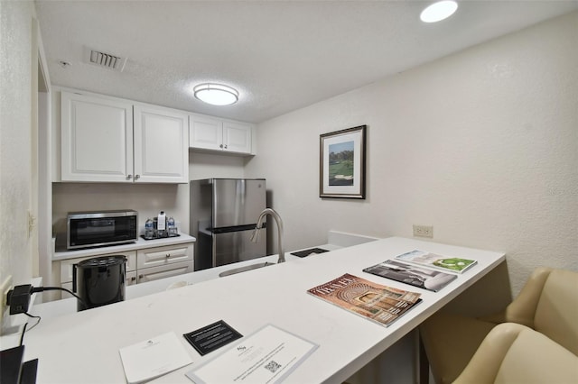 kitchen featuring kitchen peninsula, stainless steel appliances, sink, white cabinetry, and a textured ceiling