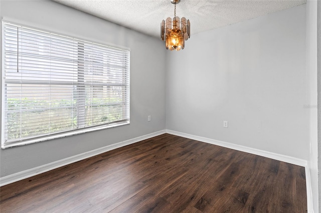 spare room featuring dark wood-type flooring, a textured ceiling, and a chandelier