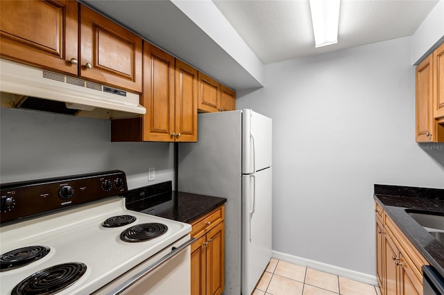 kitchen featuring light tile patterned floors, dark stone counters, and white appliances