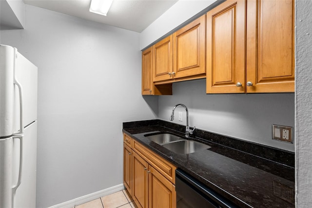 kitchen with white refrigerator, black dishwasher, dark stone counters, sink, and light tile patterned floors