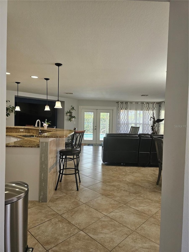 kitchen with french doors, sink, stone counters, hanging light fixtures, and a breakfast bar area