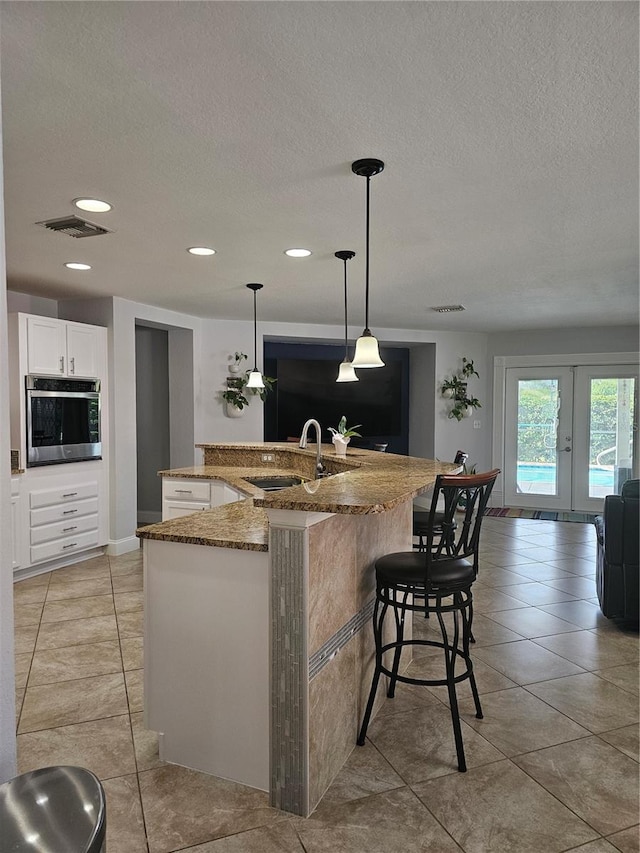 kitchen with french doors, white cabinets, oven, sink, and hanging light fixtures