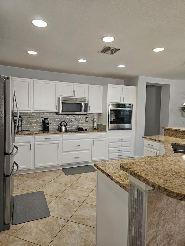 kitchen with stone counters, white cabinetry, decorative backsplash, light tile patterned flooring, and appliances with stainless steel finishes