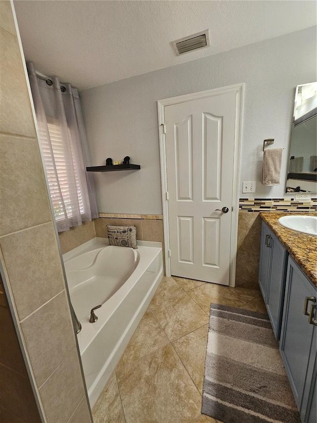 bathroom featuring vanity, tile patterned floors, a textured ceiling, a tub to relax in, and tile walls