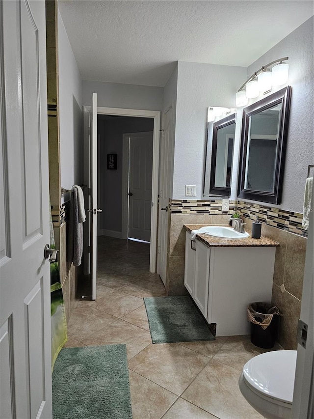 bathroom featuring vanity, a textured ceiling, tile walls, tile patterned flooring, and toilet