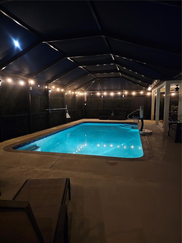 pool at twilight with glass enclosure and a patio area