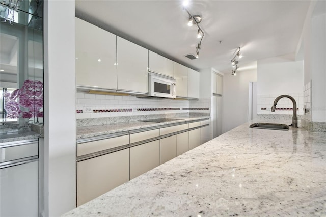 kitchen featuring black electric stovetop, backsplash, light stone countertops, and sink