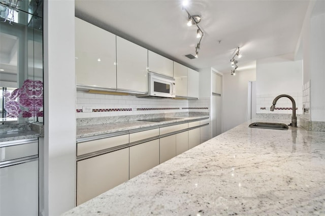 kitchen with backsplash, light stone counters, a sink, and white microwave