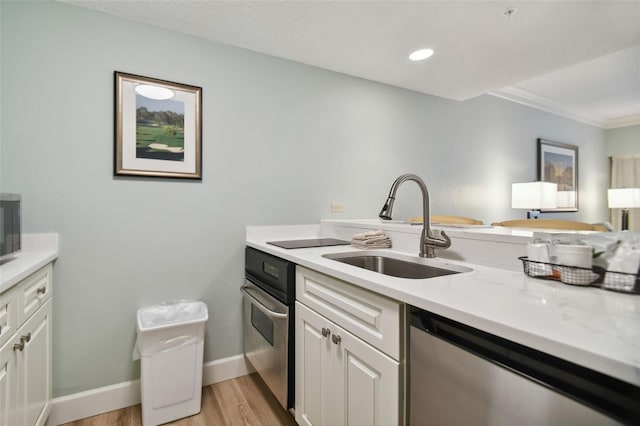 kitchen with sink, white cabinetry, stainless steel appliances, light stone counters, and light hardwood / wood-style flooring