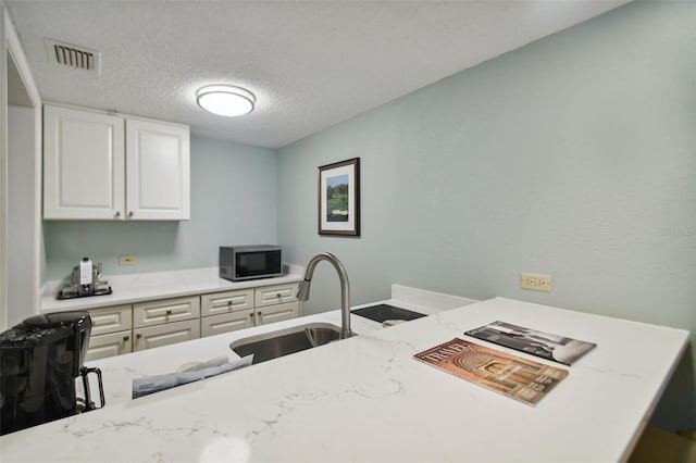 kitchen with light stone countertops, sink, white cabinetry, and a textured ceiling