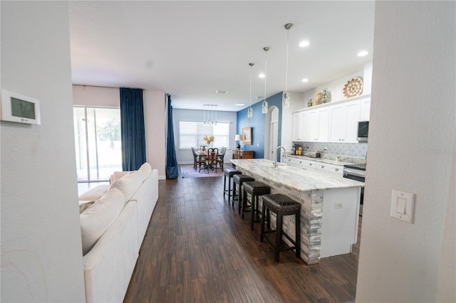 kitchen featuring decorative backsplash, a kitchen island with sink, dark hardwood / wood-style floors, a kitchen bar, and white cabinetry