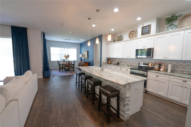 kitchen with appliances with stainless steel finishes, an island with sink, a kitchen bar, white cabinets, and dark hardwood / wood-style floors