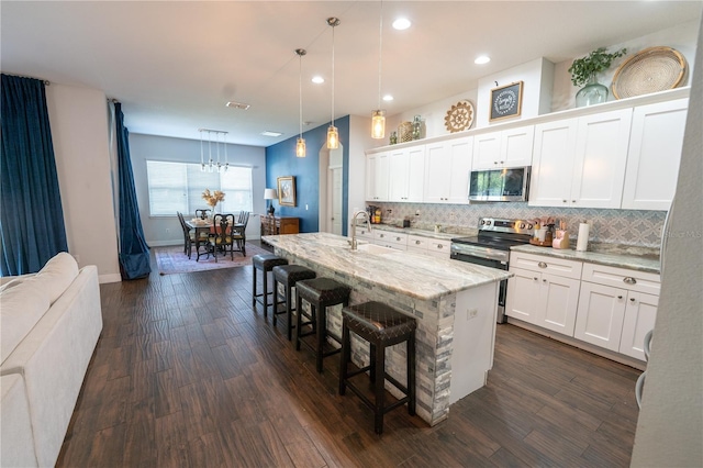 kitchen with white cabinets, dark hardwood / wood-style flooring, a kitchen breakfast bar, an island with sink, and pendant lighting