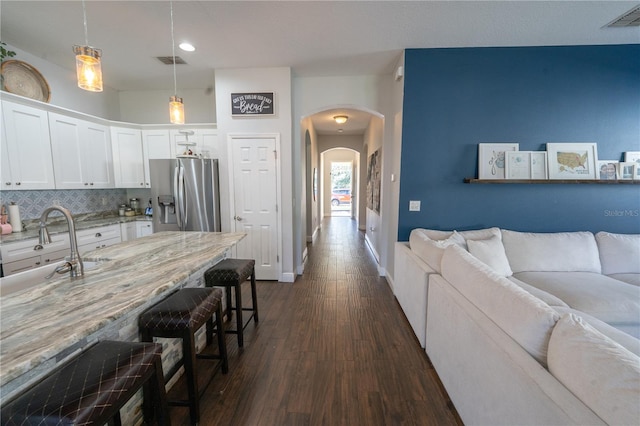 kitchen featuring dark hardwood / wood-style floors, hanging light fixtures, stainless steel fridge with ice dispenser, white cabinetry, and light stone counters