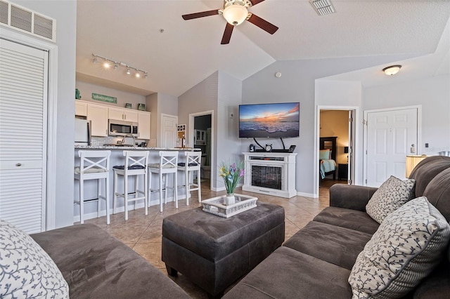 living room featuring lofted ceiling, light tile patterned flooring, a fireplace, and ceiling fan