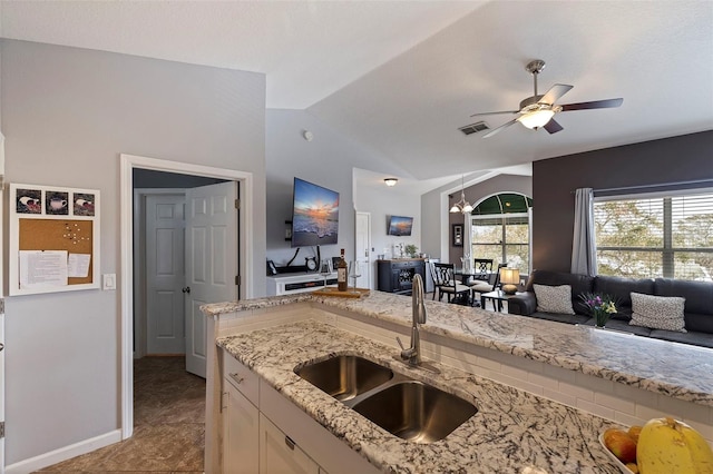 kitchen with light stone countertops, vaulted ceiling, light tile patterned flooring, ceiling fan with notable chandelier, and sink