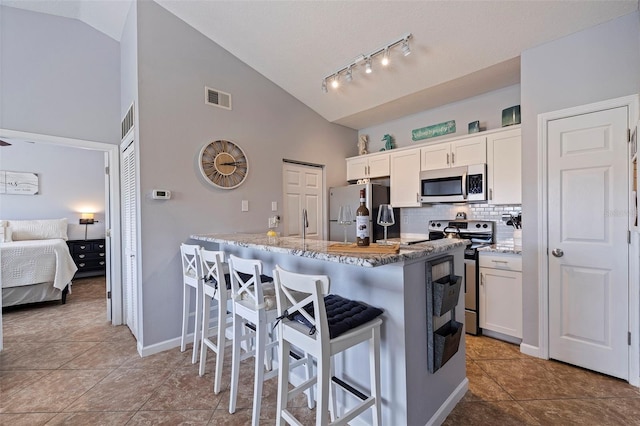 kitchen featuring appliances with stainless steel finishes, white cabinetry, a kitchen breakfast bar, and vaulted ceiling