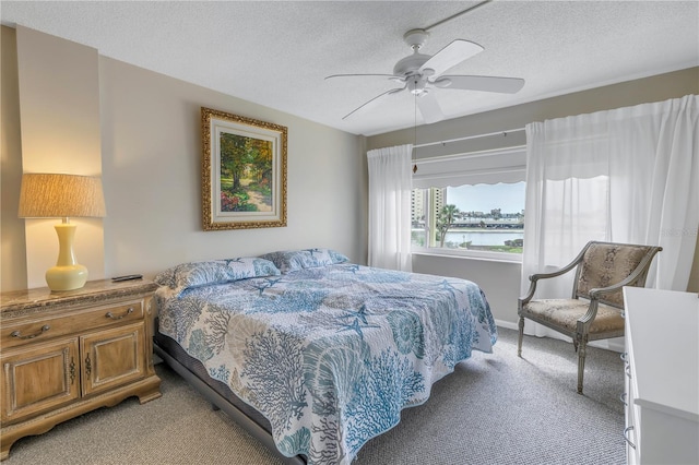 bedroom featuring ceiling fan, light colored carpet, a water view, and a textured ceiling