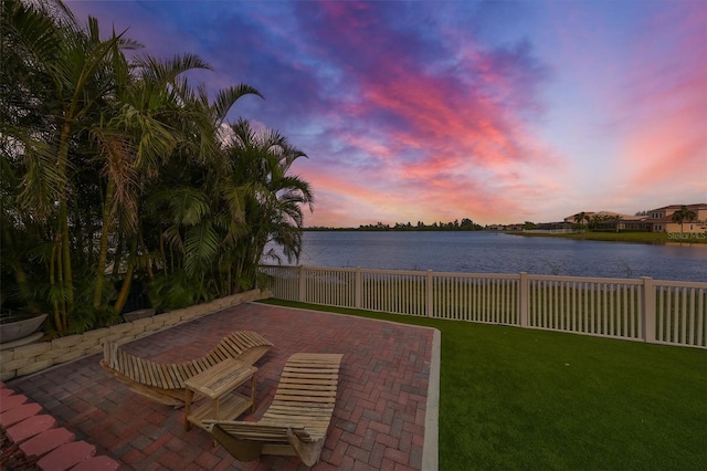 patio terrace at dusk with a water view and a lawn