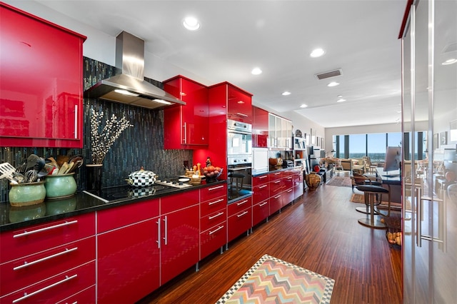 kitchen featuring black electric cooktop, wall chimney exhaust hood, decorative backsplash, visible vents, and red cabinets