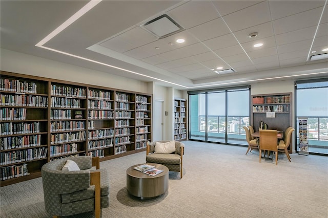 sitting room with carpet flooring, visible vents, bookshelves, and a raised ceiling