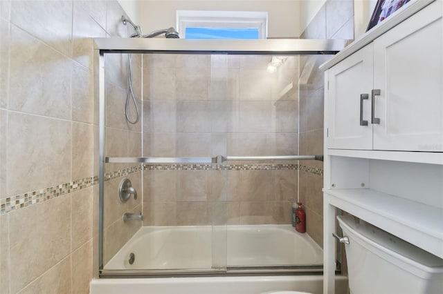 bathroom featuring toilet and shower / bath combination with glass door