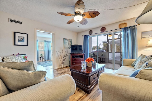 living room featuring light hardwood / wood-style flooring, a textured ceiling, and ceiling fan