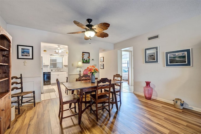 dining space with light hardwood / wood-style floors, a textured ceiling, sink, and ceiling fan