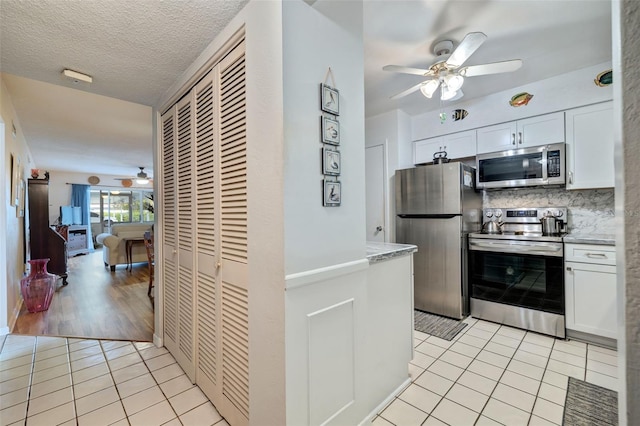 kitchen with decorative backsplash, white cabinetry, a textured ceiling, light wood-type flooring, and stainless steel appliances