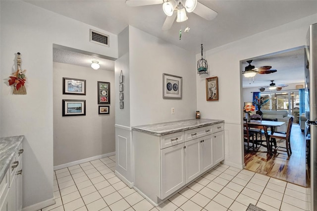 kitchen featuring stainless steel fridge, light tile patterned floors, white cabinetry, light stone counters, and ceiling fan