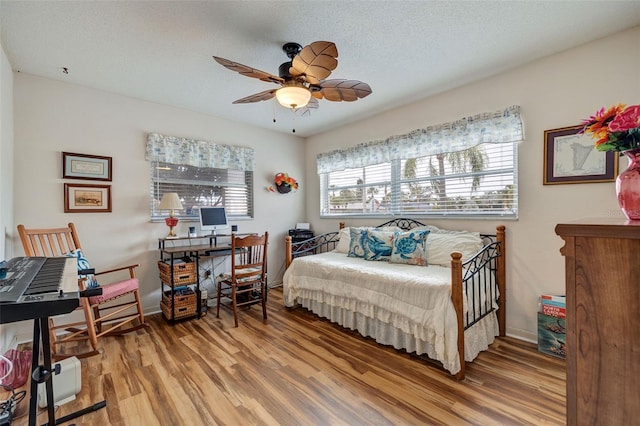 bedroom with a textured ceiling, wood-type flooring, and ceiling fan