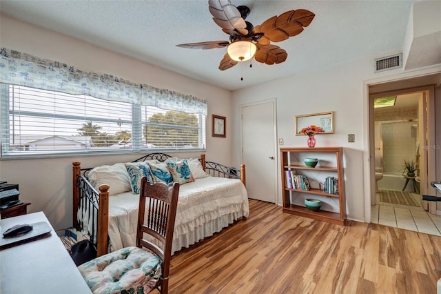 bedroom featuring connected bathroom, light hardwood / wood-style flooring, a textured ceiling, and ceiling fan