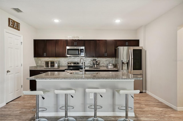 kitchen featuring light wood-type flooring, appliances with stainless steel finishes, and an island with sink