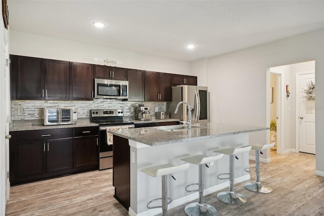 kitchen with a center island with sink, sink, a breakfast bar, appliances with stainless steel finishes, and light hardwood / wood-style floors