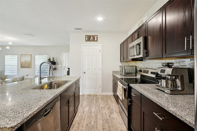 kitchen with dark brown cabinets, light stone counters, light hardwood / wood-style flooring, sink, and stainless steel appliances