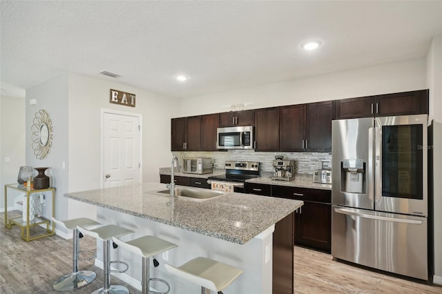 kitchen featuring appliances with stainless steel finishes, sink, light hardwood / wood-style floors, a breakfast bar area, and a center island with sink