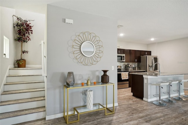 kitchen featuring light wood-type flooring, stainless steel appliances, dark brown cabinets, and a kitchen bar